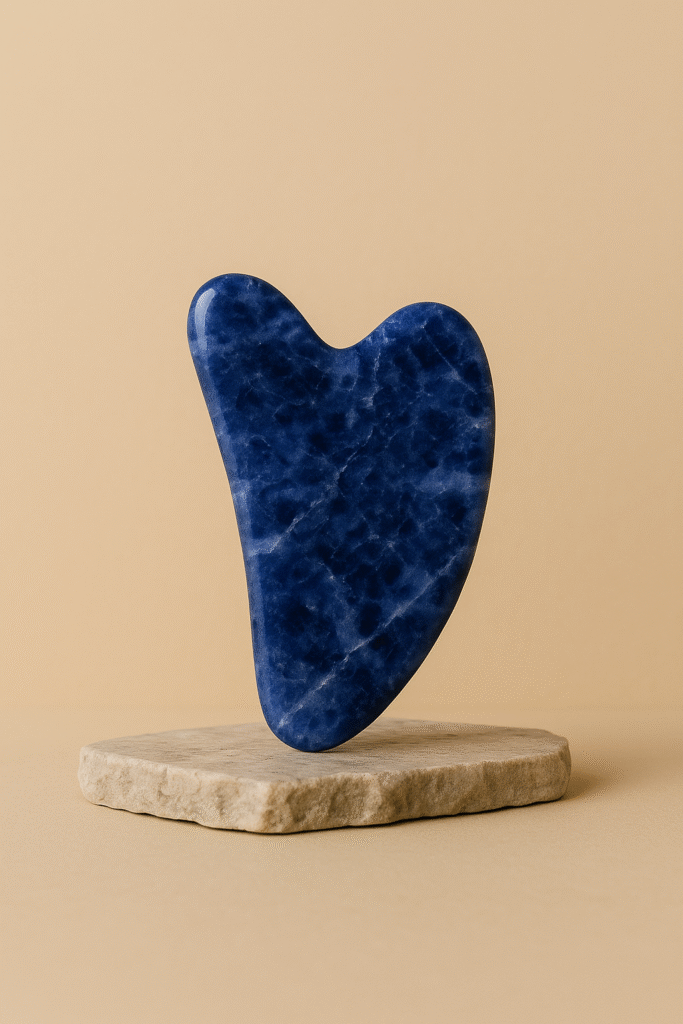 Blue sodalite gua sha stone standing upright on a beige background.
