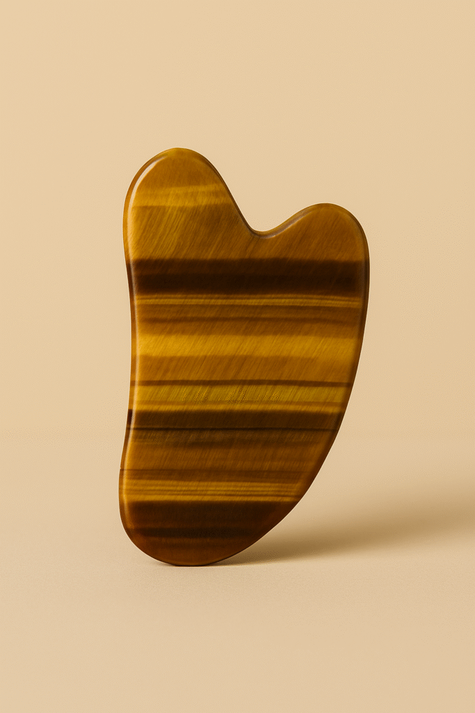 Tiger’s Eye gua sha stone standing upright on a beige background.